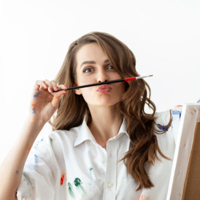 Portrait of young woman making faces and depicts mustache with help of paintbrush. Fun concept