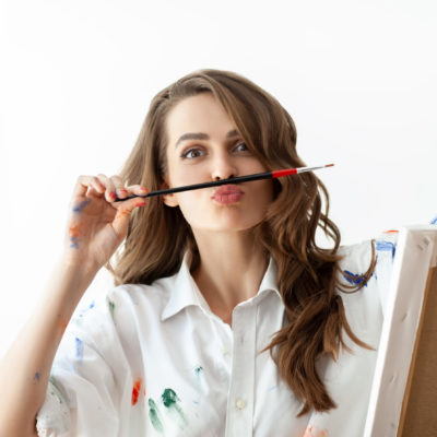 Portrait of young woman making faces and depicts mustache with help of paintbrush Portrait of young woman making faces and depicts mustache with help of paintbrush. Fun concept